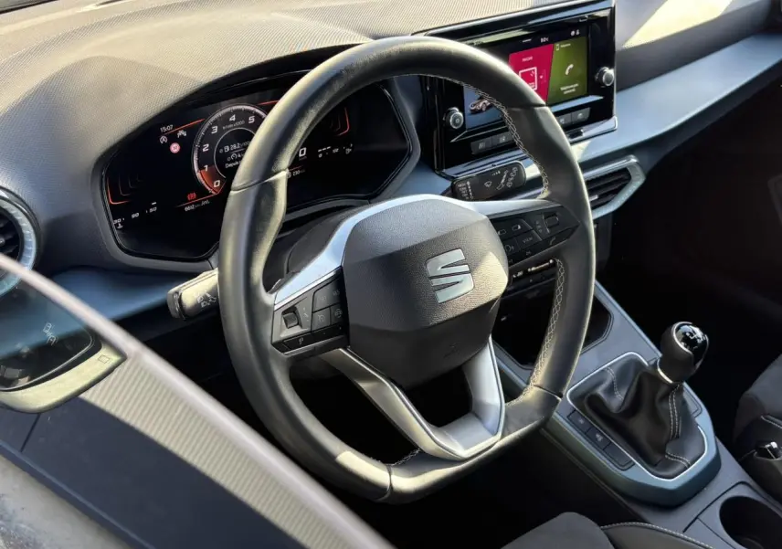 Vue rapprochée de l'intérieur du SEAT Arona TSI 115 Xpérience 2025, volant cuir multifonction et levier de vitesse manuel visibles.
