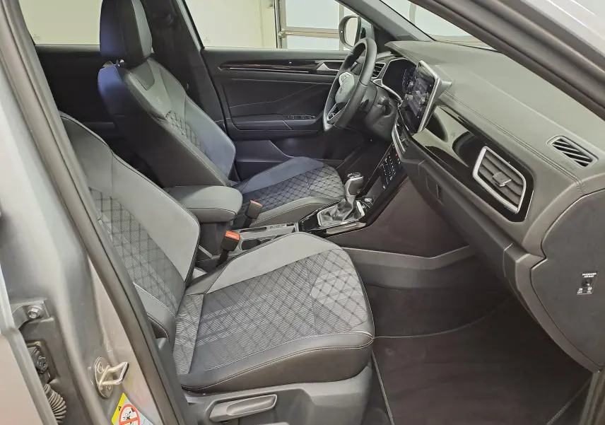 Vue intérieure côté gauche du Volkswagen T-Roc 1.5 TSI R-Line 2025, sièges tissu et alcantara gris avec console centrale.