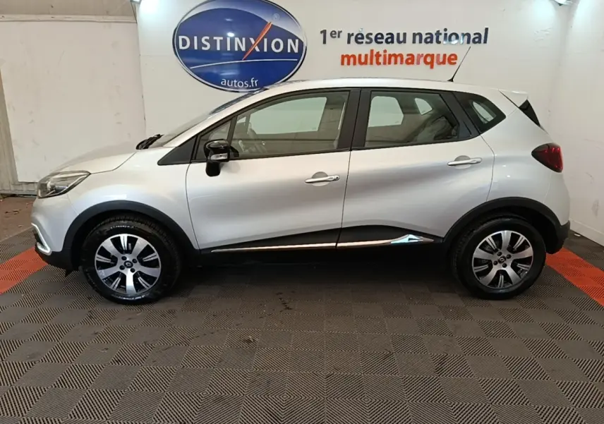 Profil droit d'un Renault Captur gris clair 2018 avec jantes alliage et rétroviseurs noirs, en intérieur showroom.