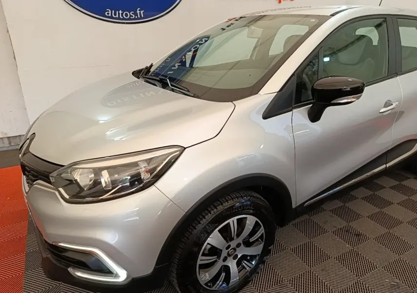 Renault Captur gris clair vu en 3/4 avant droit, avec feux à LED et rétroviseurs noirs brillants.