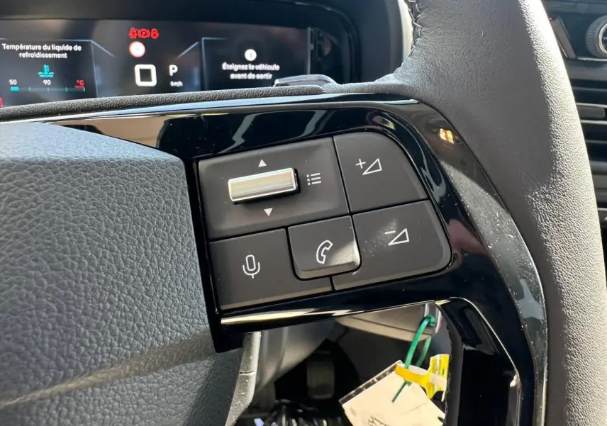 Gros plan sur les commandes multifonctions noires du volant cuir du Citroën Berlingo 2026, avec affichage digital en arrière-plan.