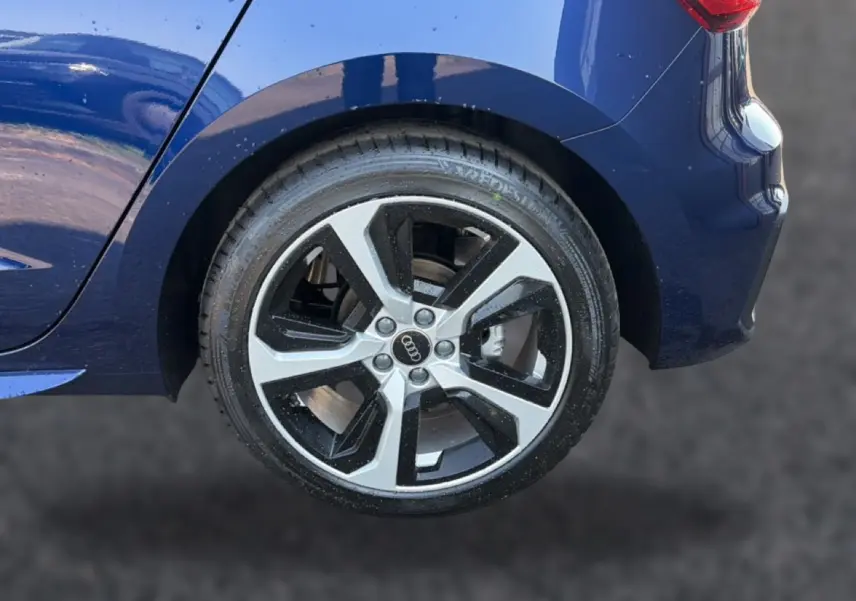 Gros plan sur la roue arrière droite d'une Audi A1 Sportback bleu foncé avec jante alu bicolore et feu arrière LED visible.