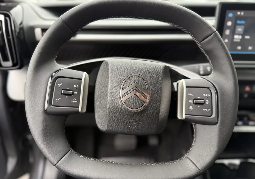 Gros plan sur le volant cuir noir du Citroën C3 hybride 2026, avec commandes intégrées et logo central chromé.