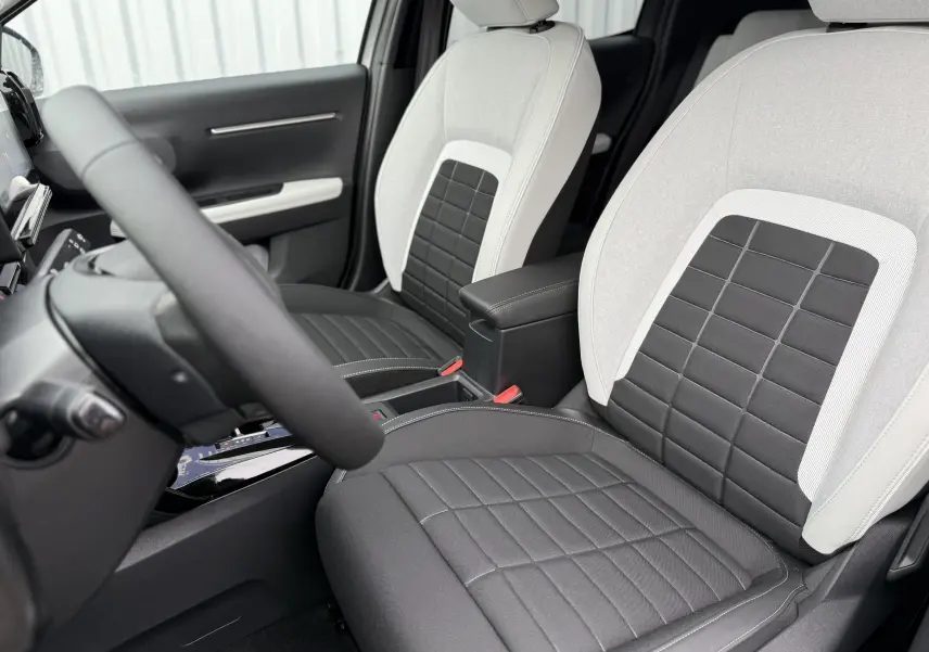 Vue intérieure côté conducteur de la Citroën C3 hybride 2026, sièges bi-ton gris clair et noir avec coutures apparentes.