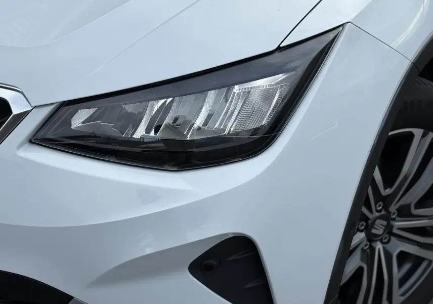 Gros plan sur le phare avant droit et la roue alliage 17'' d'un SEAT Arona blanc Nevada finition Xpérience 2025.