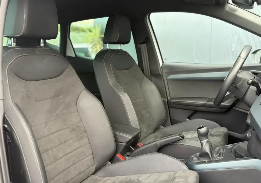 Intérieur du SEAT Arona 2025 montrant les sièges avant en tissu gris et la boîte manuelle côté droit.