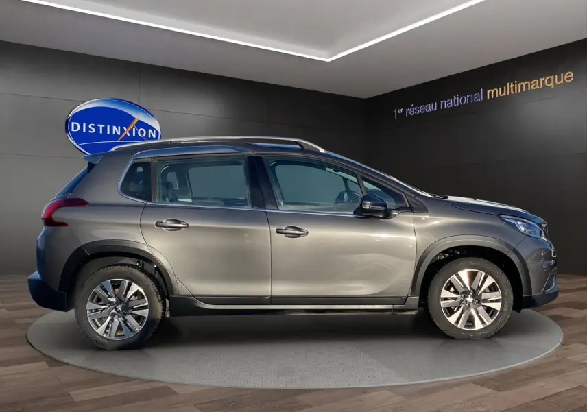 Peugeot 2008 gris platinium vue de profil côté gauche, avec jantes alliage et barres de toit visibles.