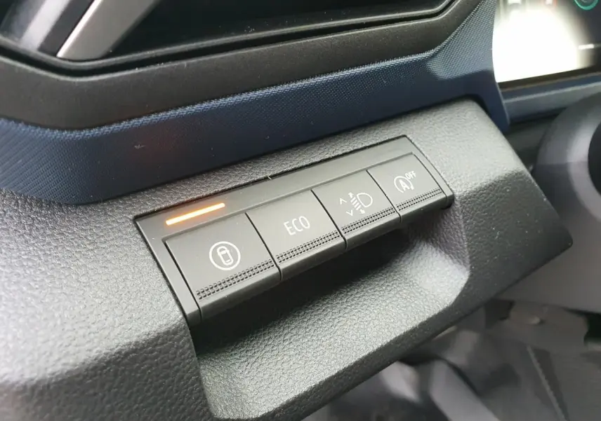 Gros plan sur les boutons de commande du tableau de bord du Dacia Duster blanc Glacier, avec témoin lumineux orange allumé.