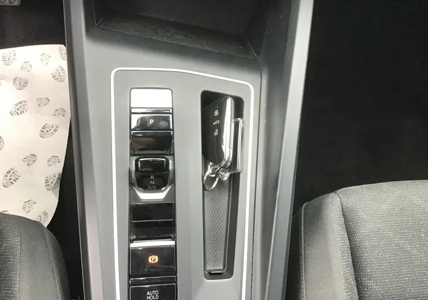 Vue plongeante sur la console centrale grise de la Volkswagen Golf VIII avec levier de vitesses DSG7 et clé mains libres posée.