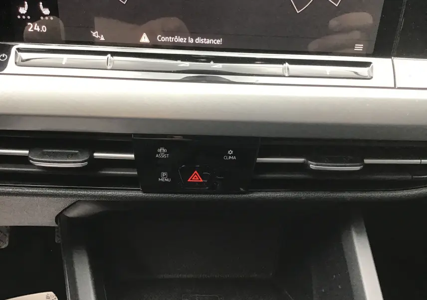 Détail du tableau de bord de la Volkswagen Golf VIII gris reflex, montrant les commandes d’assistance, climatisation et signal d’alerte.