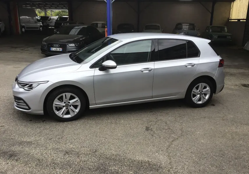 Vue de profil côté gauche d’une Volkswagen Golf VIII gris reflex garée sur sol béton, avec jantes alliage 16 pouces.