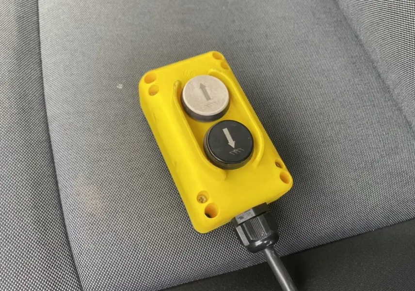 Gros plan sur la télécommande jaune avec deux boutons fléchés, posée sur un siège gris du Renault Master blanc.
