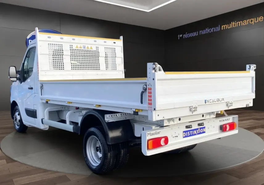 Vue 3/4 arrière droite du Renault Master blanc version benne avec ridelles et hayon, sur fond intérieur showroom.