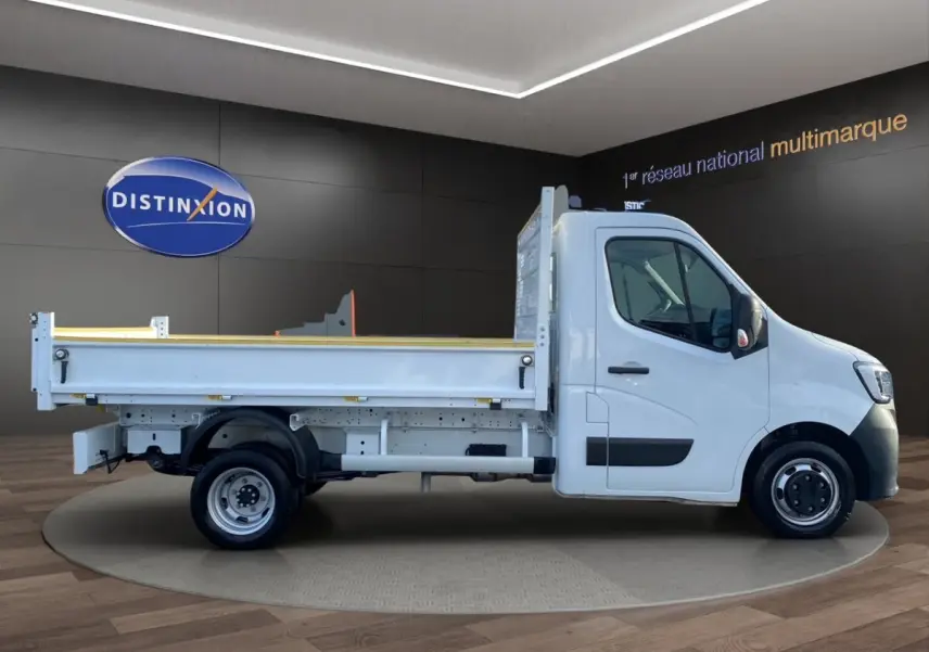 Renault Master benne blanc vu de profil côté droit dans un showroom avec sol en bois et mur noir.