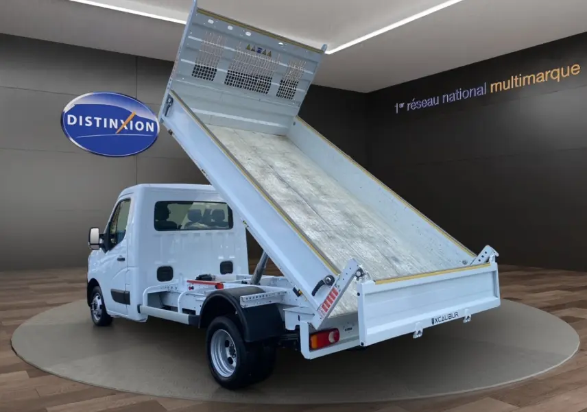 Vue 3/4 arrière d’un Renault Master blanc 2024 avec benne basculante relevée dans un showroom.