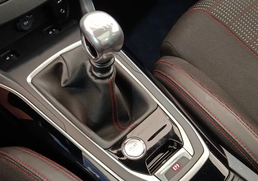 Gros plan sur la console centrale noire avec levier de vitesse manuel et bouton démarrage, sièges tissu noir à surpiqûres rouges.