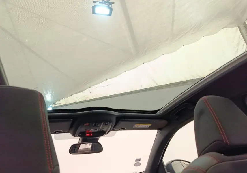 Vue intérieure du toit ouvrant panoramique et des appuis-tête noirs avec surpiqûres rouges d'une Peugeot 308 GT Line noire.