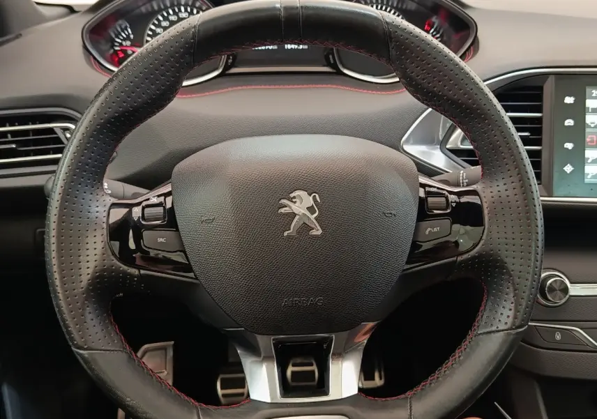 Vue rapprochée du volant cuir noir perforé avec surpiqûres rouges de la Peugeot 308 GT Line 2016, tableau de bord en arrière-plan.