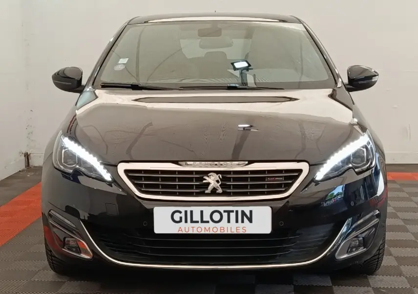Vue frontale d'une Peugeot 308 noire avec feux LED allumés et calandre chromée distinctive.