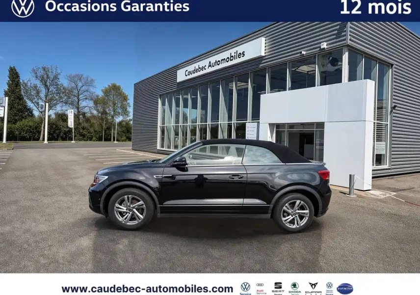 Profil droit du Volkswagen T-Roc Cabriolet noir avec capote fermée, jantes alliage et arrière du bâtiment en arrière-plan.