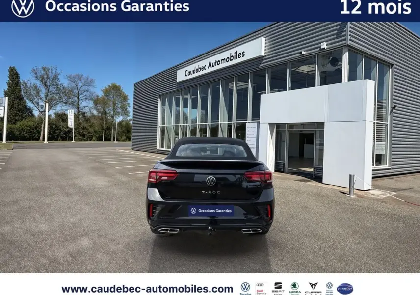 Vue arrière d'un Volkswagen T-Roc Cabriolet noir, avec attelage amovible et feux arrière LED, devant un showroom.