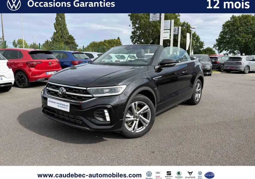 Volkswagen T-Roc Cabriolet noir en 3/4 avant droit sur parking, capote ouverte et jantes alliage visibles.