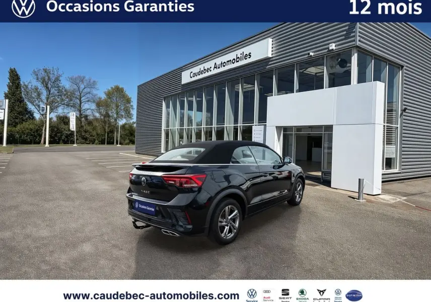 Volkswagen T-Roc Cabriolet noir vue 3/4 arrière droit, toit fermé, stationné devant un bâtiment moderne.