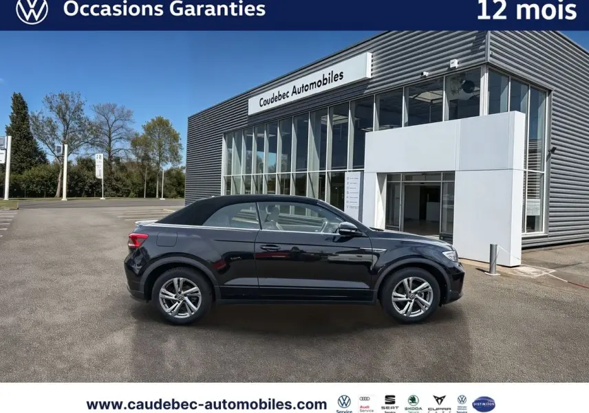 Profil droit du Volkswagen T-Roc Cabriolet noir avec toit fermé, garé devant un showroom moderne.