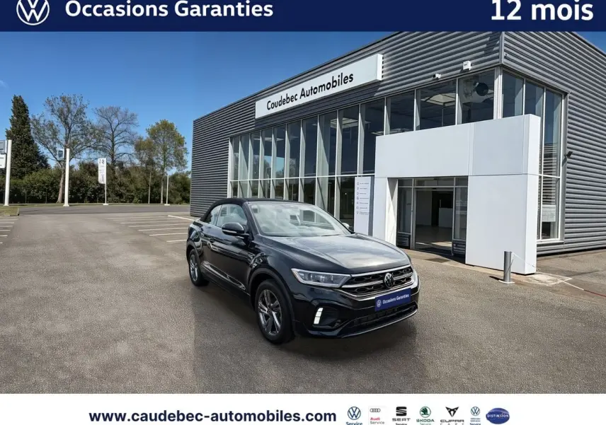 Volkswagen T-Roc Cabriolet noir en 3/4 avant droit devant un bâtiment de concession Caudebec Automobiles.