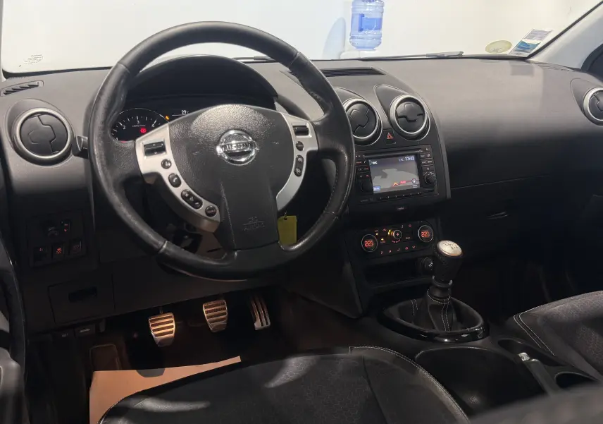 Intérieur du Nissan Qashqai+2 2014 en vue avant, volant multifonction et boîte manuelle visibles, finition Tekna gris.
