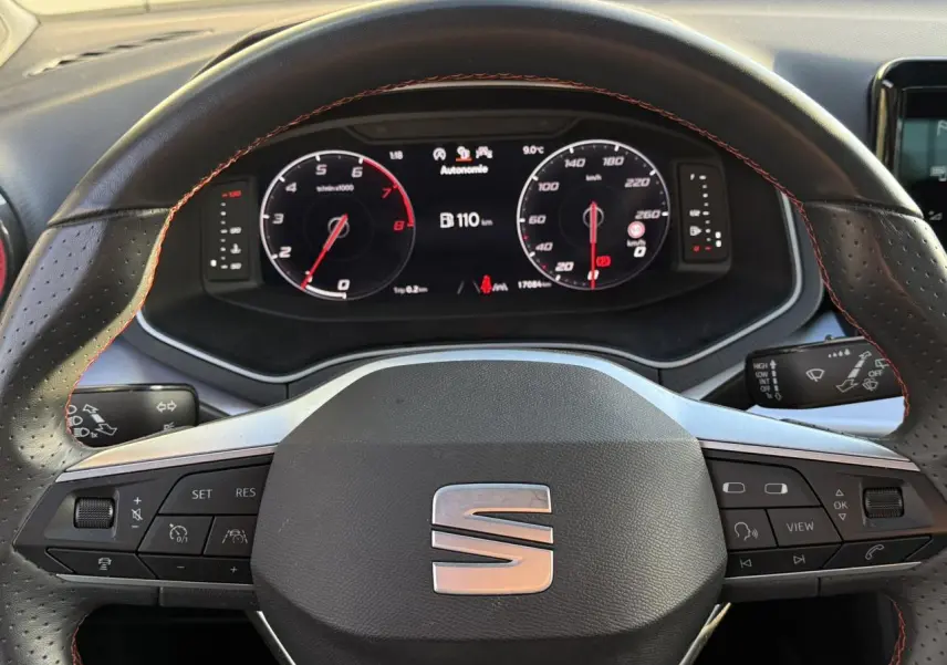 Vue rapprochée du volant en cuir noir avec surpiqûres rouges et tableau de bord digital de la SEAT IBIZA TSI 115 FR.