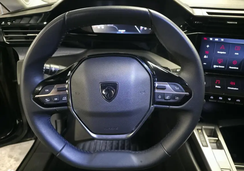 Vue rapprochée du volant noir cuir de la Peugeot 308 SW 2024 avec commandes intégrées et écran tactile à droite.