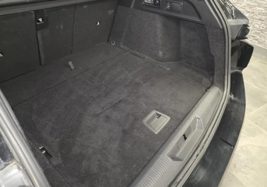 Coffre ouvert vu de l'arrière droit d'une Peugeot 308 SW noire, avec plancher plat et revêtement noir.