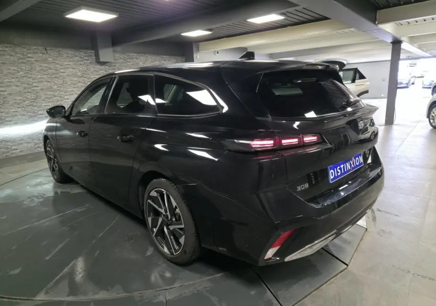 Peugeot 308 SW noire vue 3/4 arrière droit en intérieur, avec feux arrière LED et jantes alliage 17 pouces.