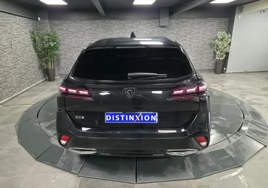 Vue arrière d'une Peugeot 308 SW noire 2024 avec feux LED allumés et logo lion distinctif au centre.