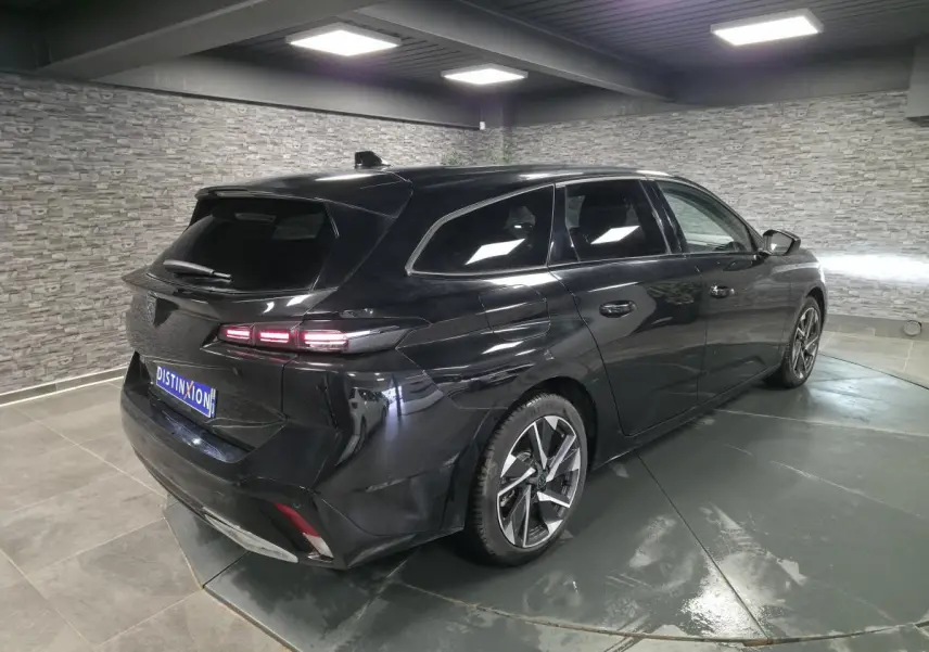 Peugeot 308 SW noire vue en 3/4 arrière droit dans un showroom avec jantes alliage et vitres surteintées.