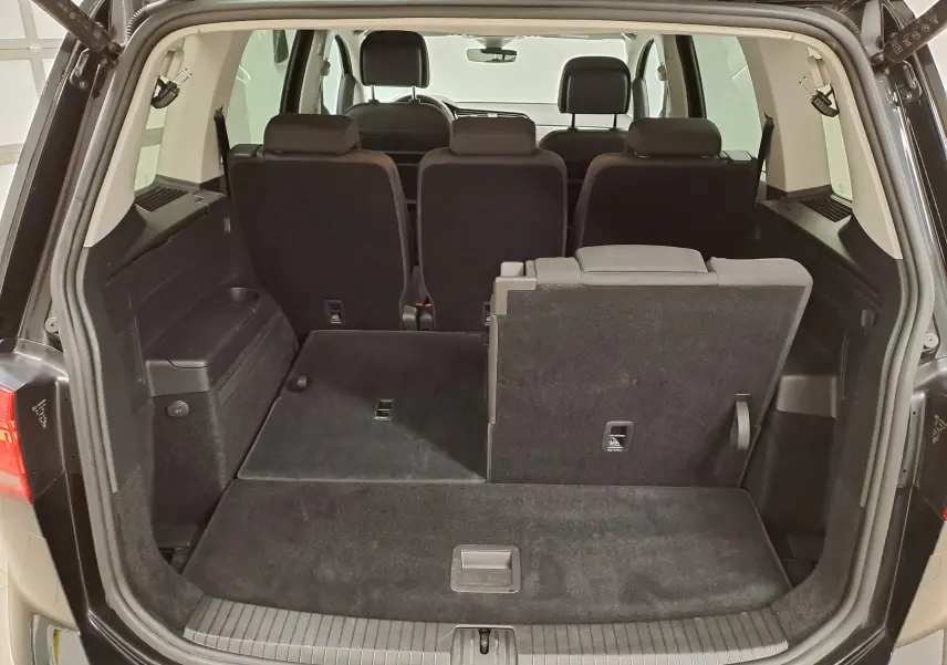 Vue arrière du coffre ouvert du Volkswagen Touran noir intense nacré, montrant les sièges arrière rabattables en partie.