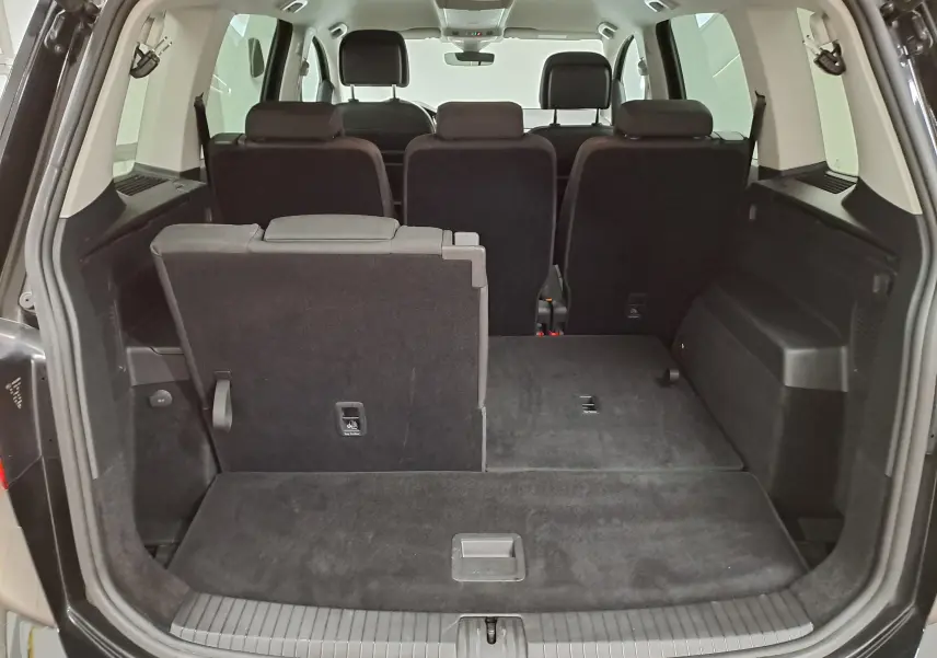 Vue arrière du coffre ouvert du Volkswagen Touran noir intense nacré, montrant les sièges arrière partiellement rabattus.