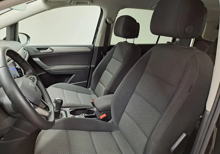Vue intérieure côté conducteur du Volkswagen Touran 2025, sièges tissu gris et tableau de bord moderne.