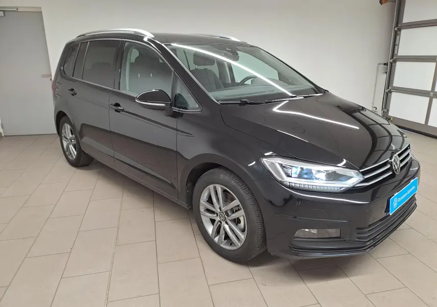 Volkswagen Touran 2025 noir nacré en 3/4 avant droit avec phares allumés dans un garage intérieur.