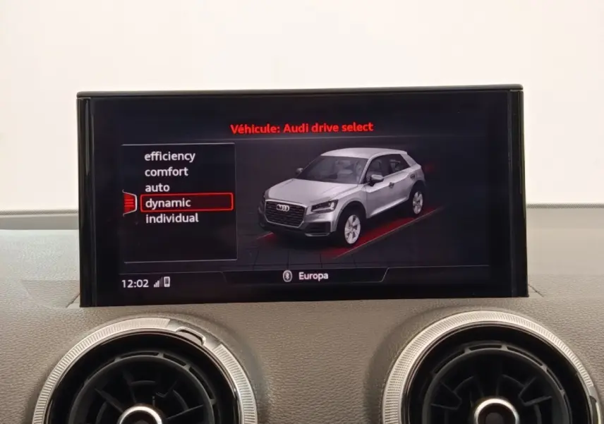 Écran central affichant le mode Audi drive select avec un SUV Q2 gris en vue 3/4 avant, entouré de commandes d’aération rondes.