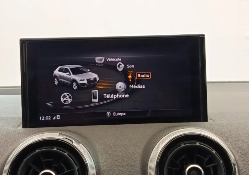 Écran tactile central affichant le menu multimédia d’un Audi Q2 noir, avec deux aérateurs ronds en dessous.