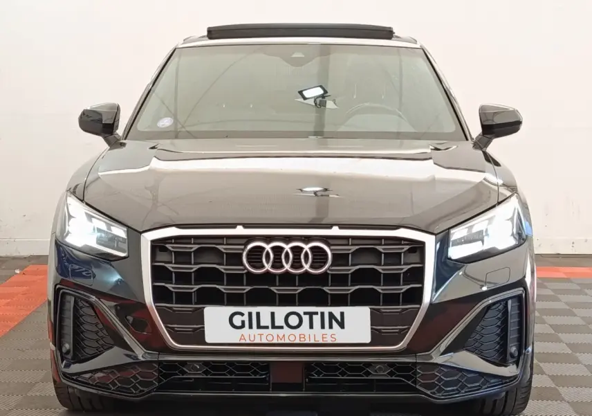Vue frontale d’un Audi Q2 noir 2021 avec calandre hexagonale et phares LED allumés dans un showroom.