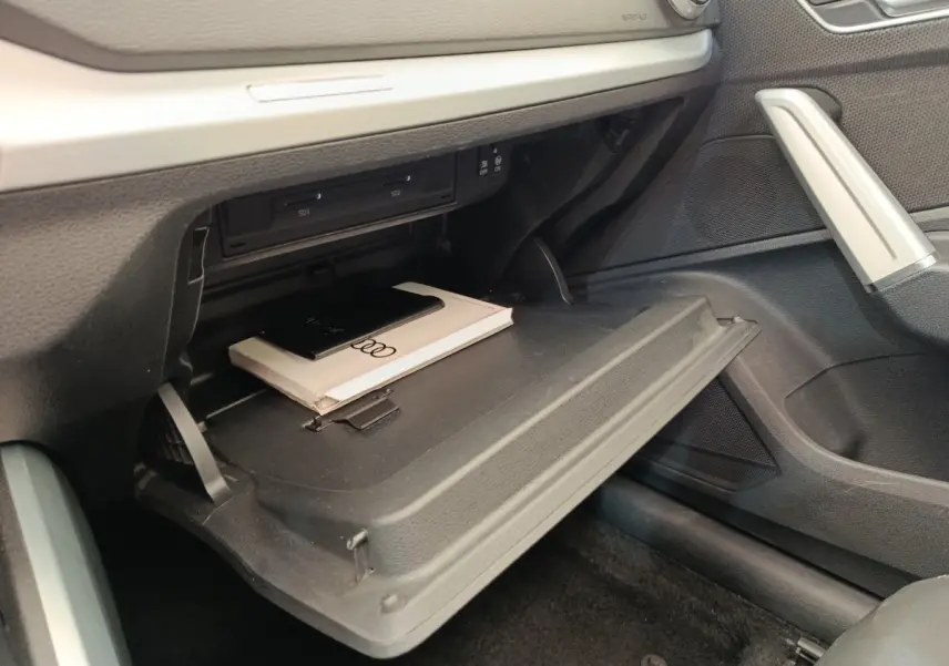 Gant de boîte à gants ouvert côté passager dans l'Audi Q2 noir, avec manuel et porte-CD visibles.