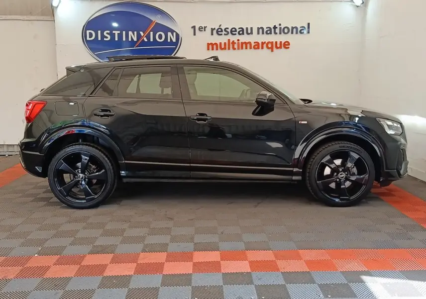 Profil côté gauche d'un Audi Q2 noir 35 TFSI S Line 2021 avec jantes noires dans un showroom multimarque.