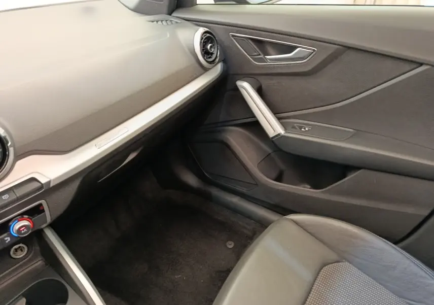 Intérieur côté passager de l’Audi Q2 35 TFSI noir, montrant la porte, siège et tableau de bord minimaliste.