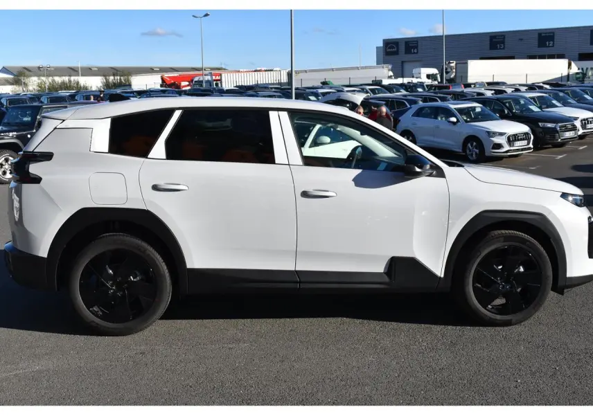 Profil droit d'un Citroën C5 Aircross blanc 2026 avec jantes noires et vitres arrière surteintées sur parking.