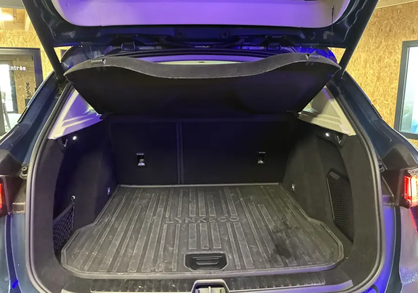 Coffre ouvert vu de l'arrière d'un Lynk & Co 01 bleu, avec tapis de coffre noir marqué Lynk & Co.