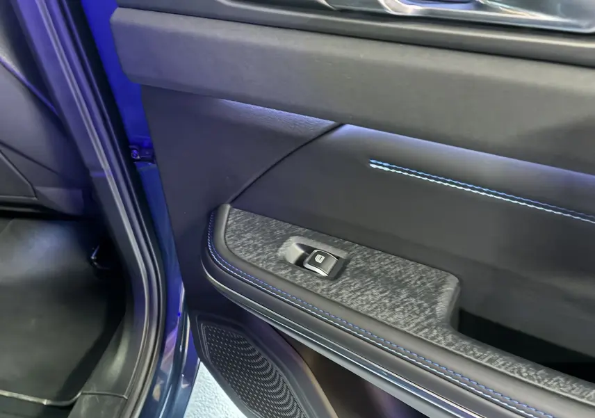 Vue rapprochée de la porte arrière gauche bleu du Lynk & Co 01 2023 avec couture bleue et bouton de lève-vitre.