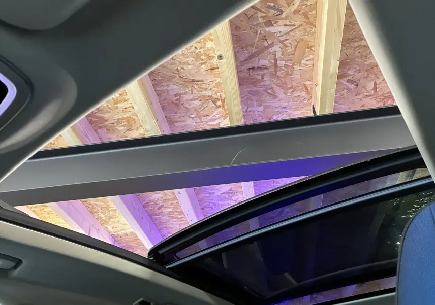 Toit panoramique ouvert vu de l'intérieur sur un LYNK & CO 01 bleu avec ciel de garage en bois visible.